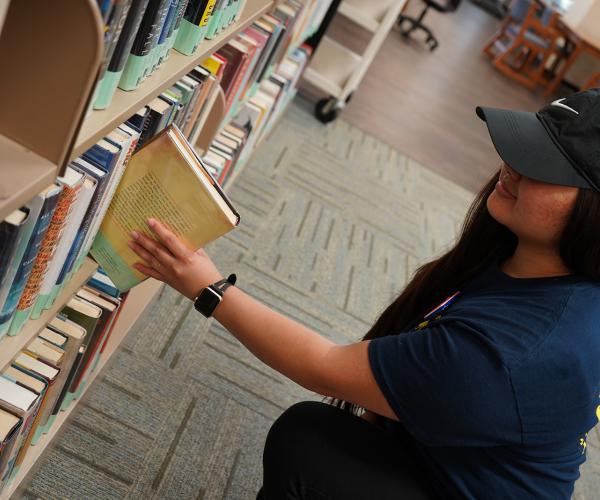 Student pulling popular reading book off shelf