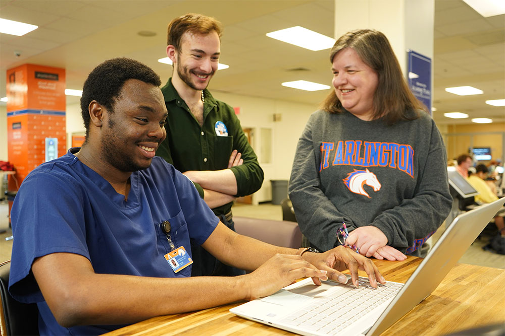 two students look at a computer while a supervisor offers assistance