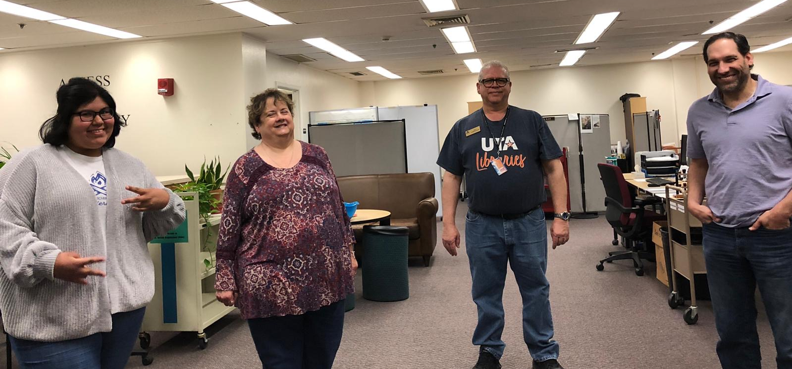 four people stand in the library basement and smile at the camera