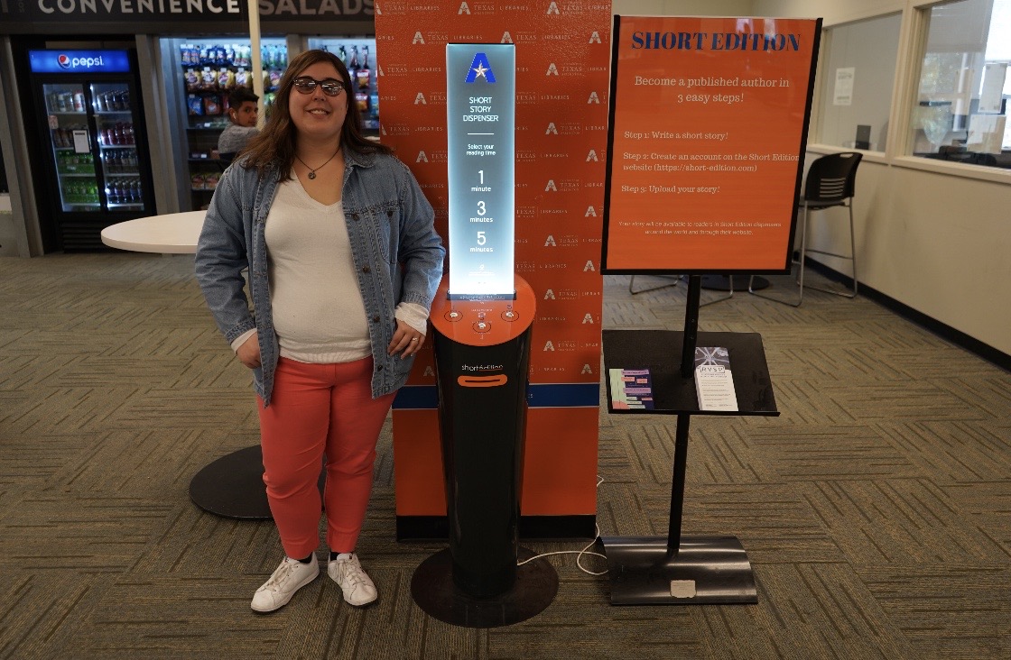 a young woman stands beside a short edition short story dispenser on the second floor of central library