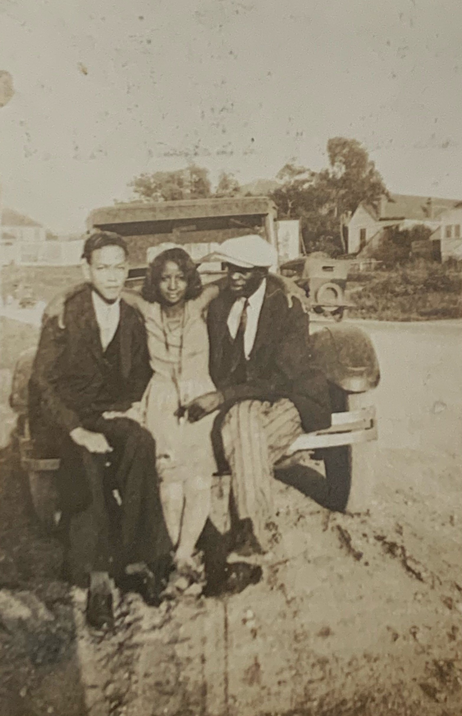Two men and a woman pose on an automobile