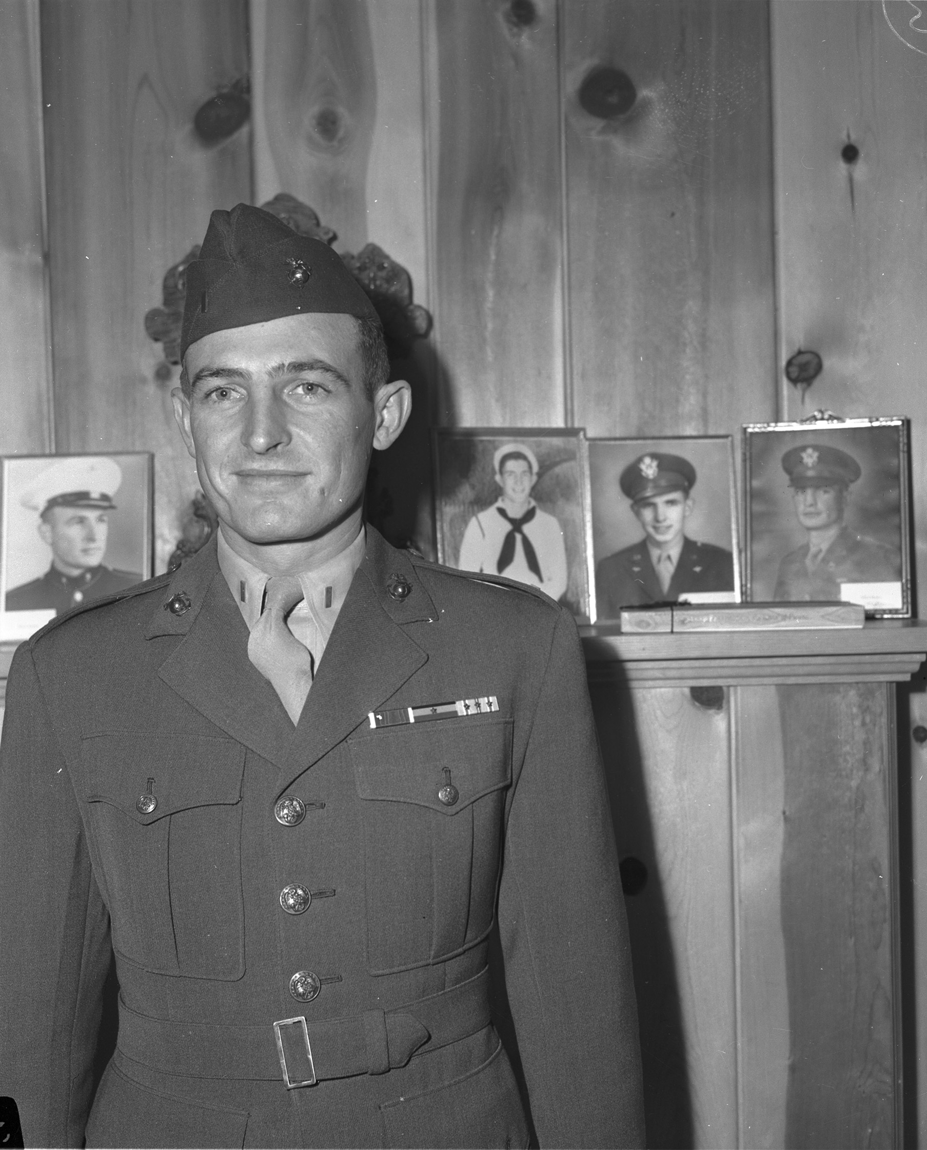 Robert Boydstun in uniform standing in front of photographs of his brothers.