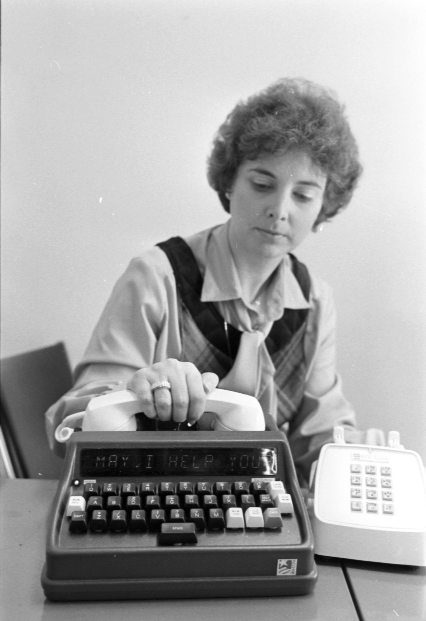 This photograph, from the Dallas-Fort Worth Airport's Community Services office, depicts a woman setting down a telephone receiver. The telephone was built to be accessible and usable for Deaf and Hard of Hearing users. February 1981.