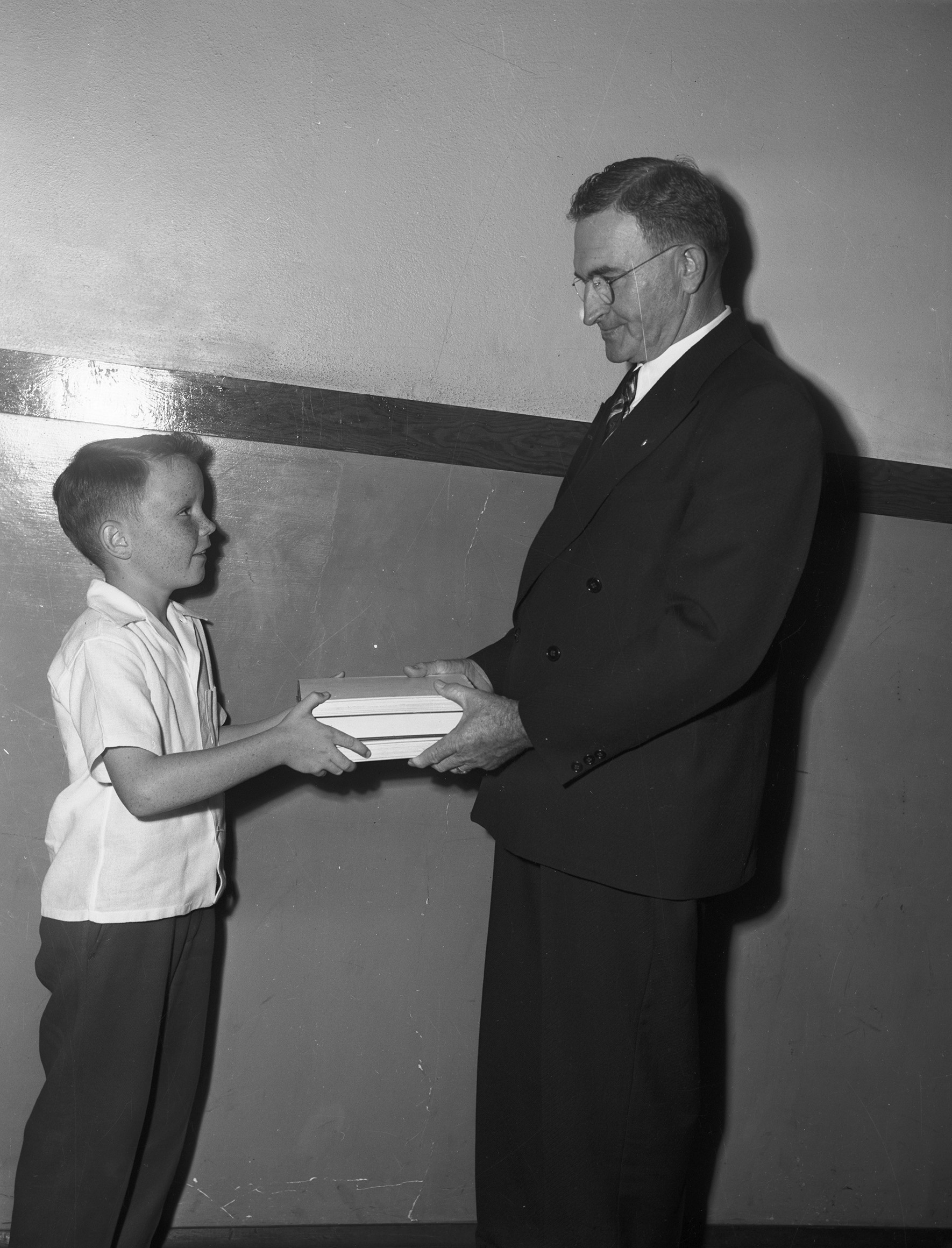 James Jennings, left, fifth grade pupil at Diamond Hill School, accepts a gift of books from J. J. Boydstun as a memorial to his former classmate, Walter Leon Pool. James is wearing a shirt and trousers and Mr. Boydstun is wearing a suit and eyeglasses.