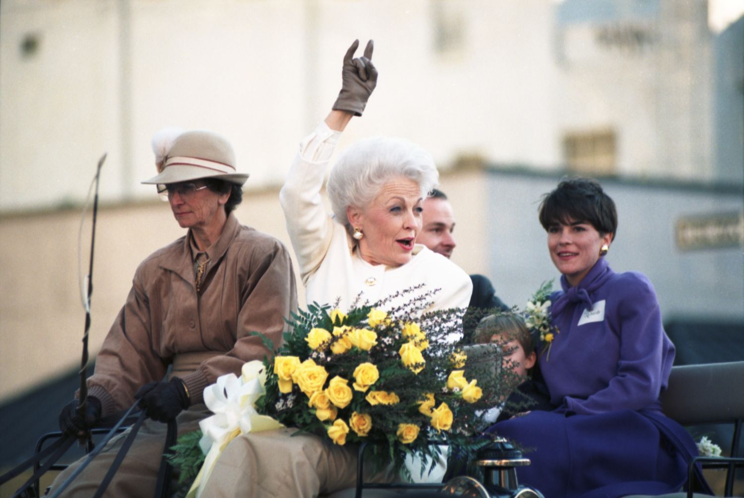  Inauguration of Texas Governor Ann Richards in Austin, Texas. Richards is seen in a horse-drawn carriage, carrying a bouquet of yellow roses and gesturing with up a "Hook 'Em" Texas Longhorns sign with her right hand. Richards' youngest daughter, Ellen Richards, is seen seated behind her in a purple coat.