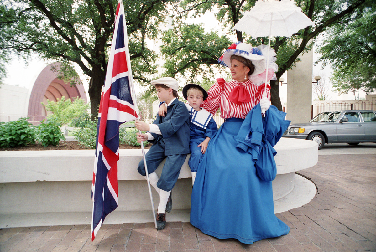 A woman and two young boys are seen in costume with one of the boys holding a Union Jack British flag in honor of Queen Elizabeth II's visit to Dallas.
