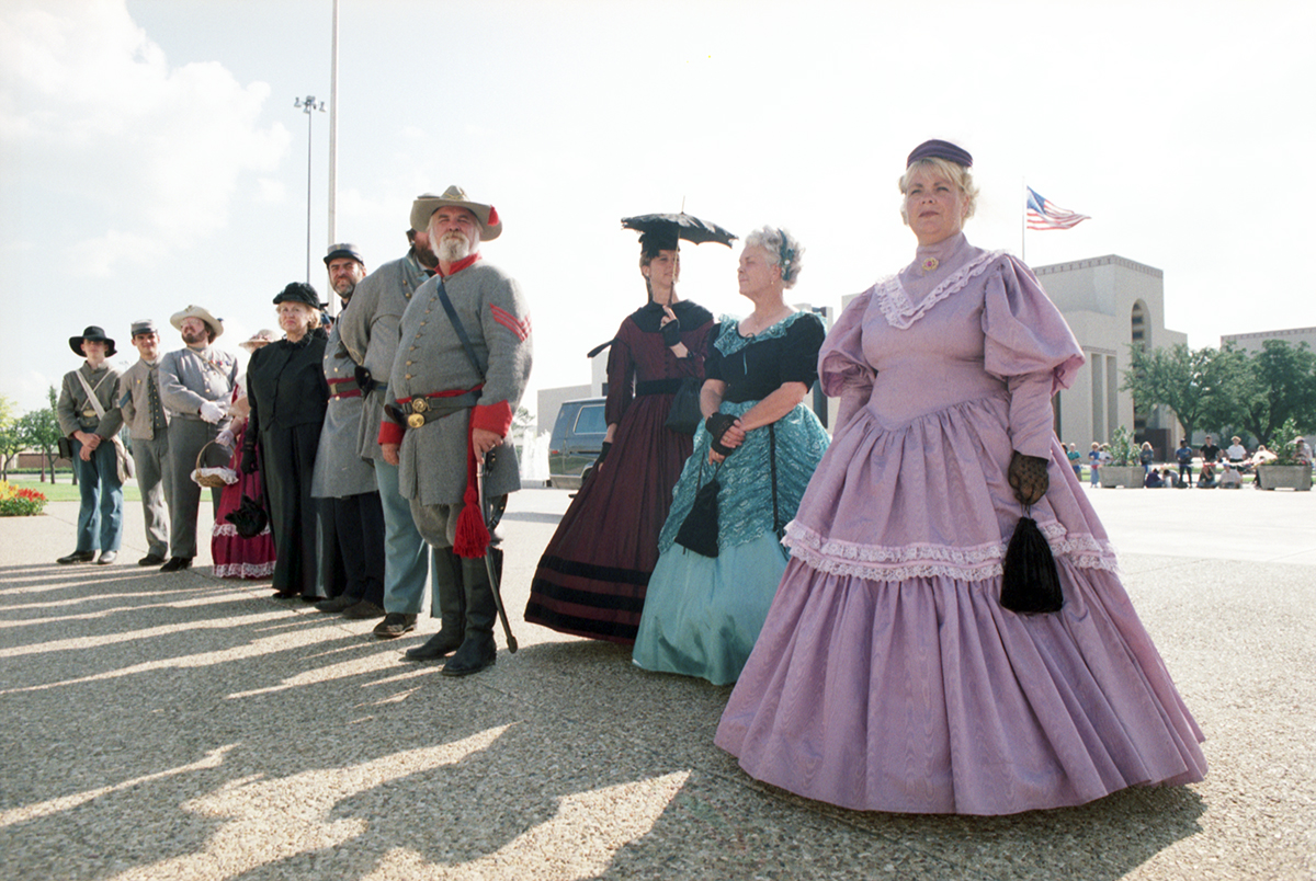 People dressed in period clothing, possibly from the Victorian era, and Confederate soldiers uniforms are seen outside of the Hall of State in downtown Dallas in honor of Queen Elizabeth II's visit to Dallas.