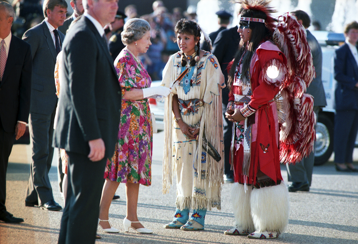 Queen Elizabeth II accepting a gift from people dressed in traditional Native American clothing.