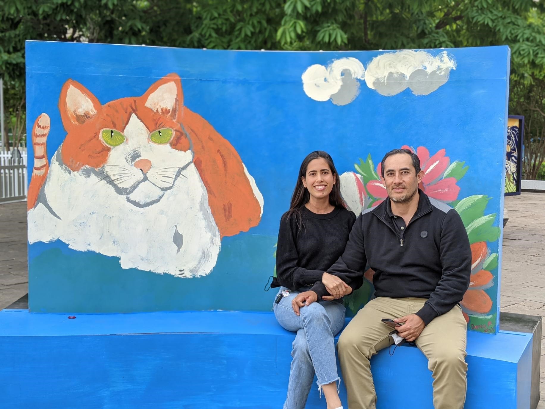 a man and woman sit in front of a mural featuring a white and orange cat on a blue background