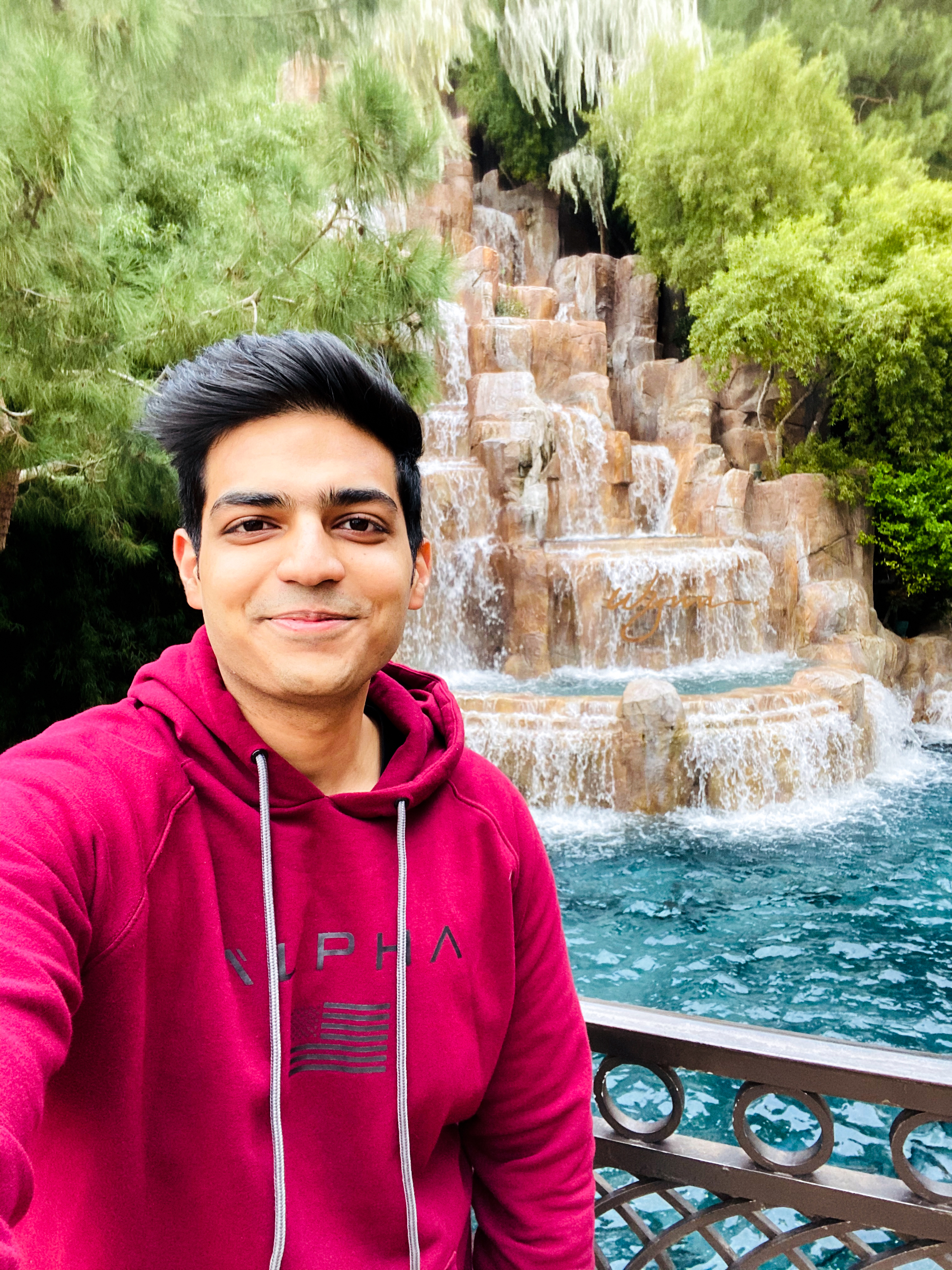 a young man smiles at the camera and poses in front of a waterfall