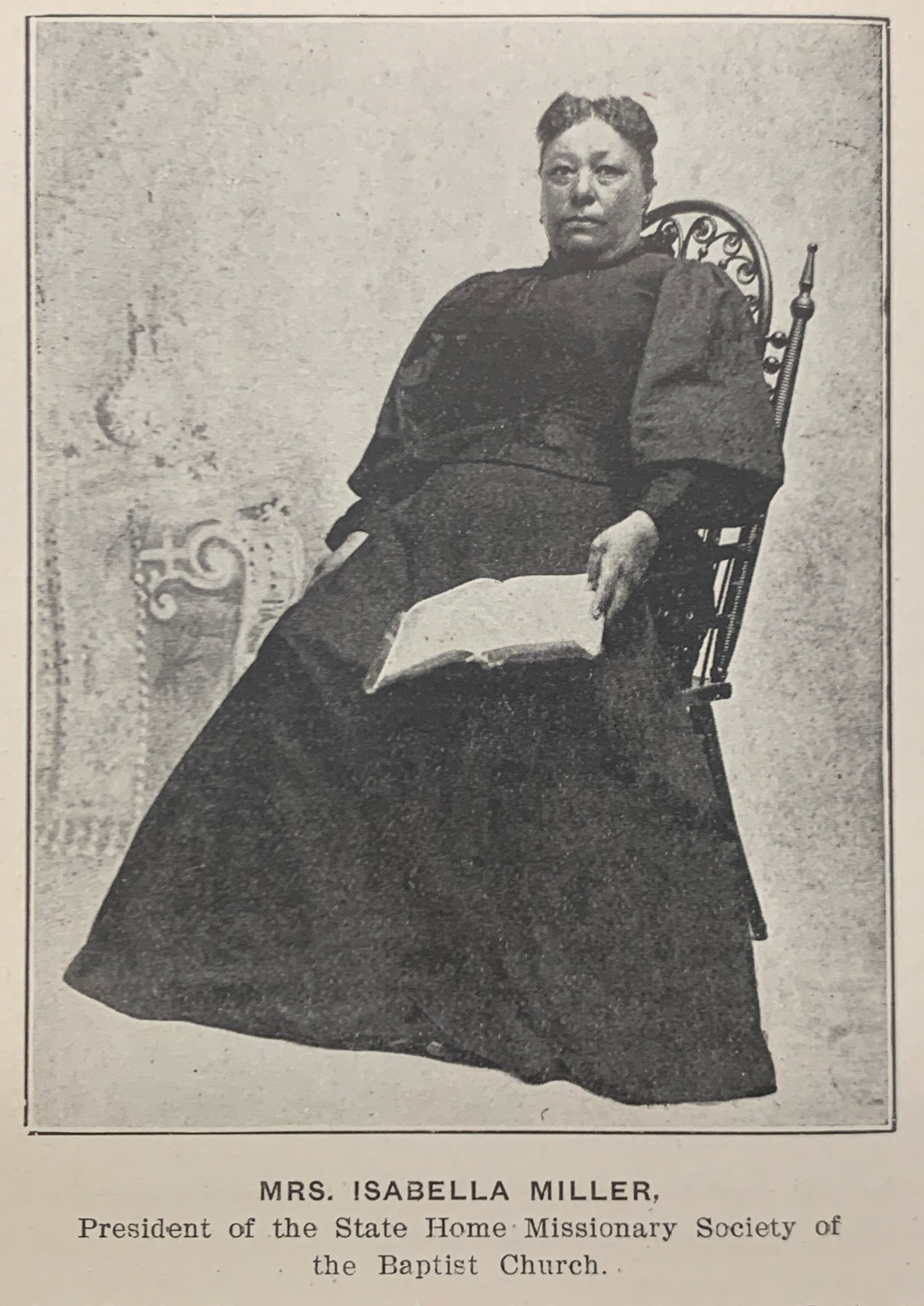 An African-American woman wearing an 1900's style dress sitting on a chair, with an open book on her lap. Text reads: Mrs. Isabella Miller, President of the State Home Missionary Society of the Baptist Church.