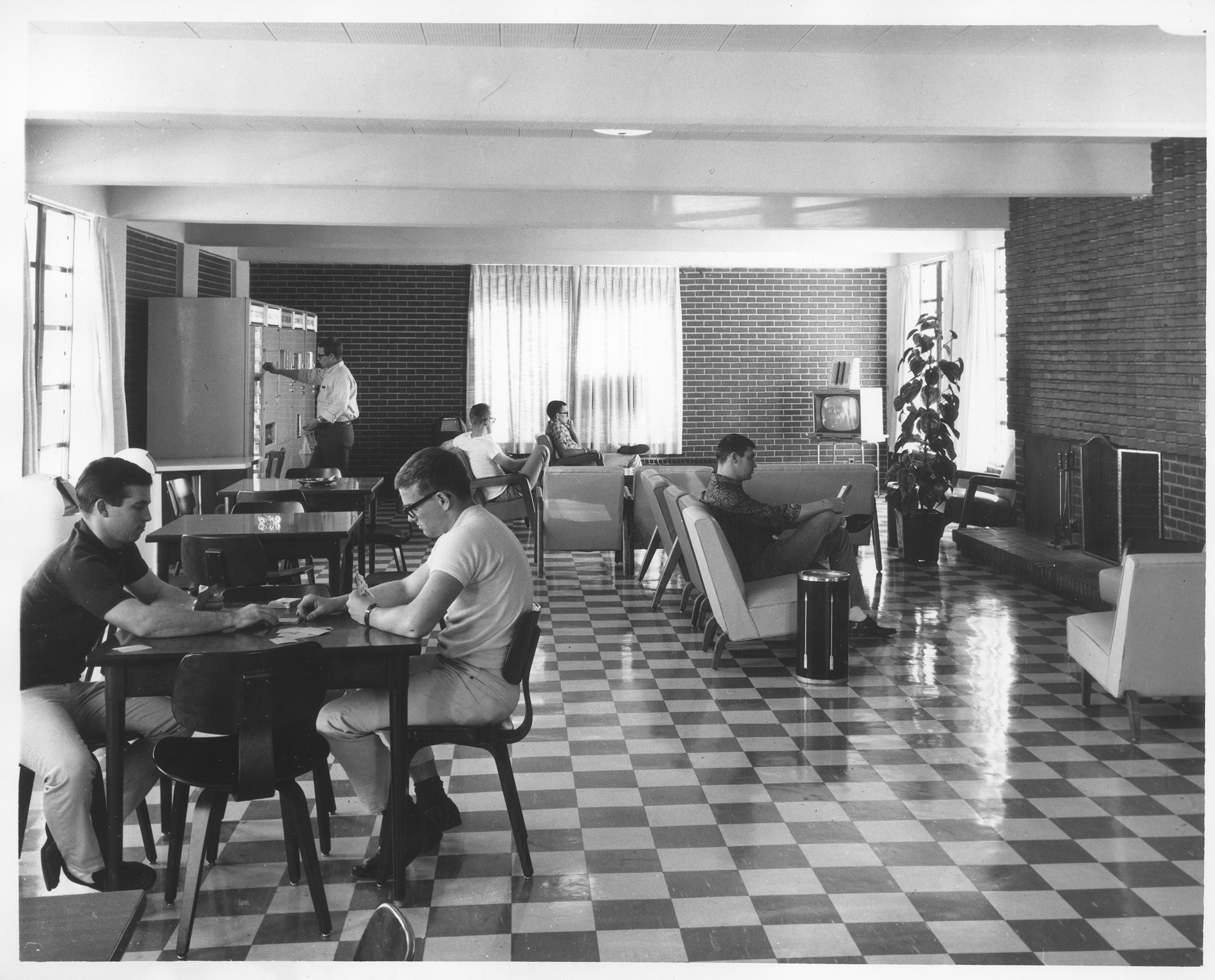 Building interior with students at tables and on couches. The walls are made of brick and there is a checkerboard-patterned floor.