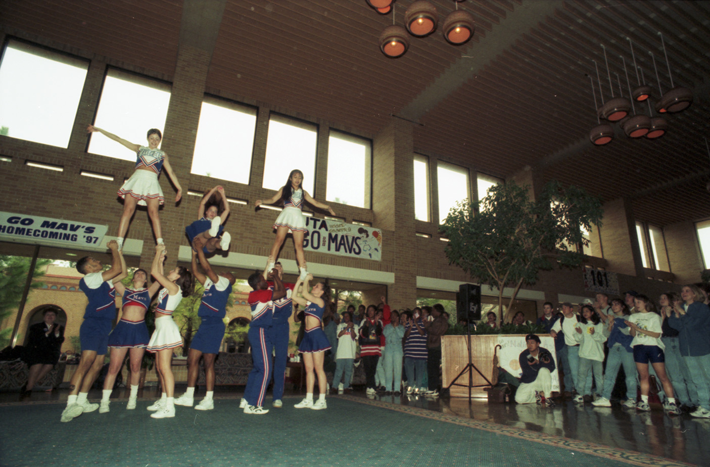 Cheerleaders performing inside the University Center with a crowd in the background.