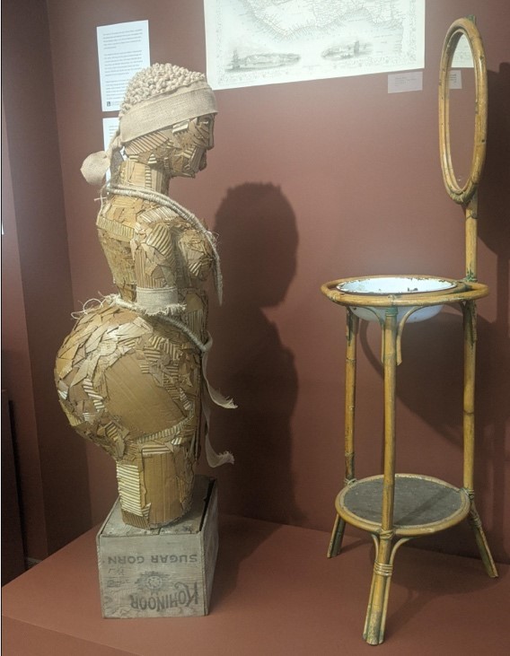 Statue of woman made from paper products, looking in a mirror