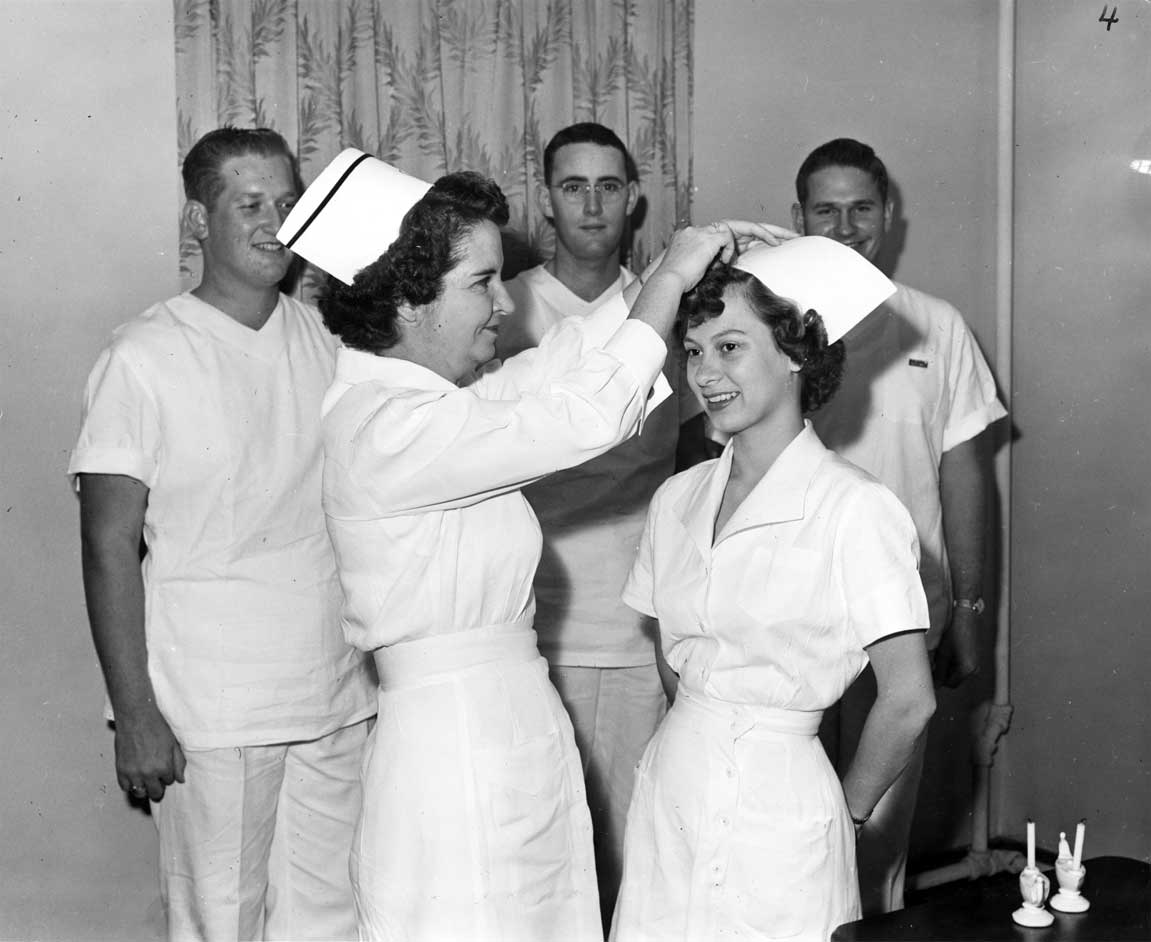 Nurse receiving a cap during a capping ceremony, while three male nurses look on