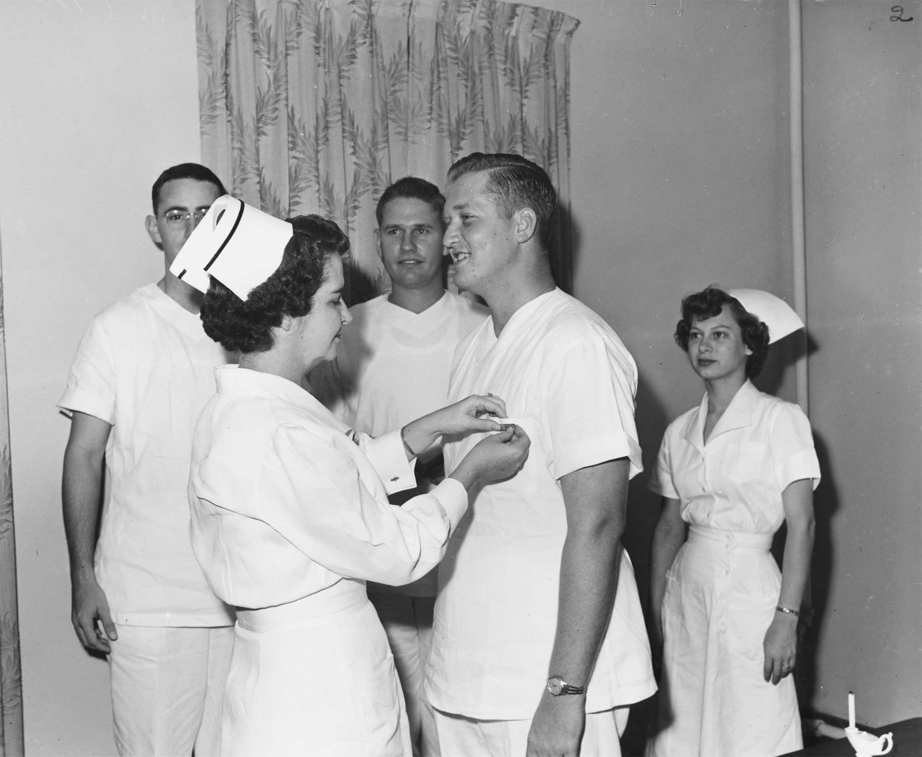 Male nurse receiving a pin during a capping ceremony, while three nurses look on