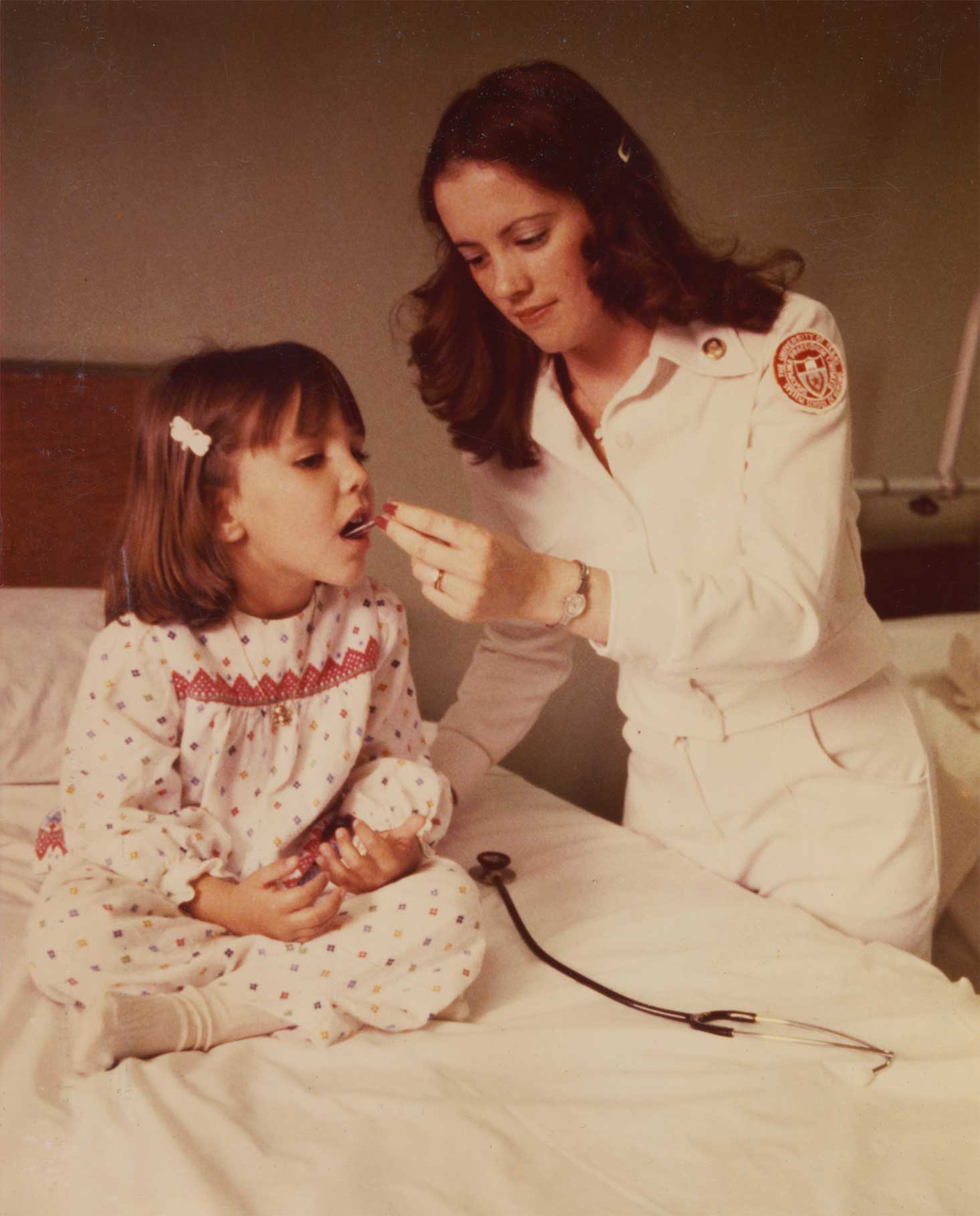 Nurse taking the temperature of a girl sitting on a hospital bed.