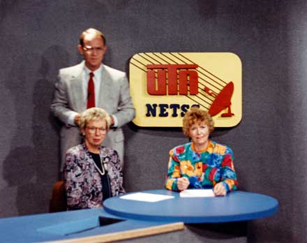 Two sitting women and one man standing on a TV set, with the "UTA NETSS" logo on the wall