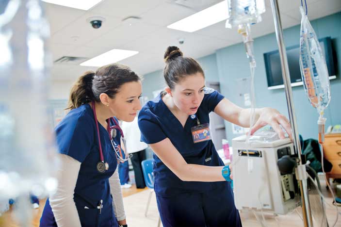 Two nurses wearing scrubs programming an IV pump in a clinical setting