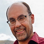 Head shot showing man wearing glasses and wearing a red shirt smiling. 
