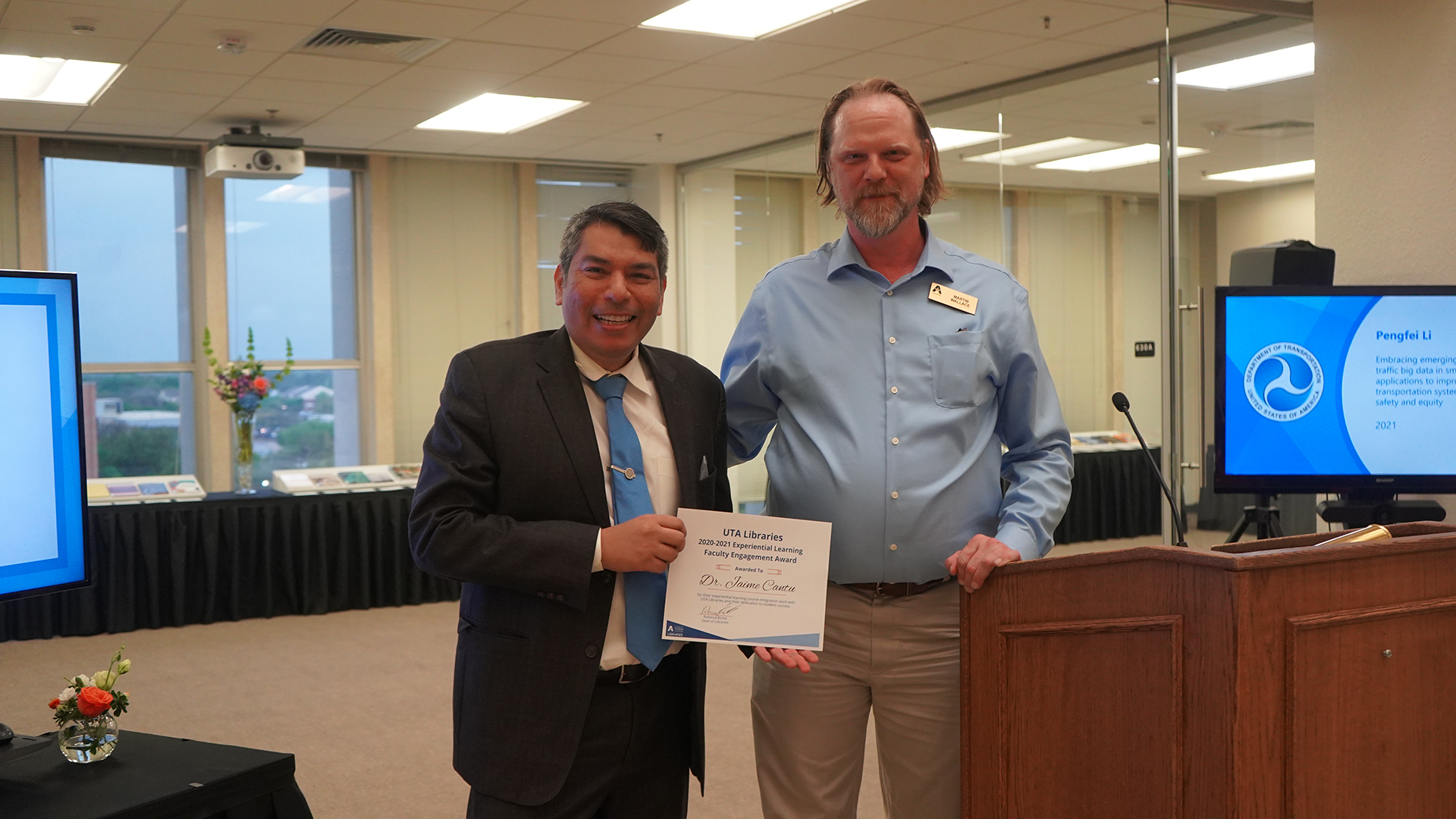 Dr. Jaime Cantu and Experiential Learning Librarian Martin Wallace pose with a paper award in the Atrium of Central Library.