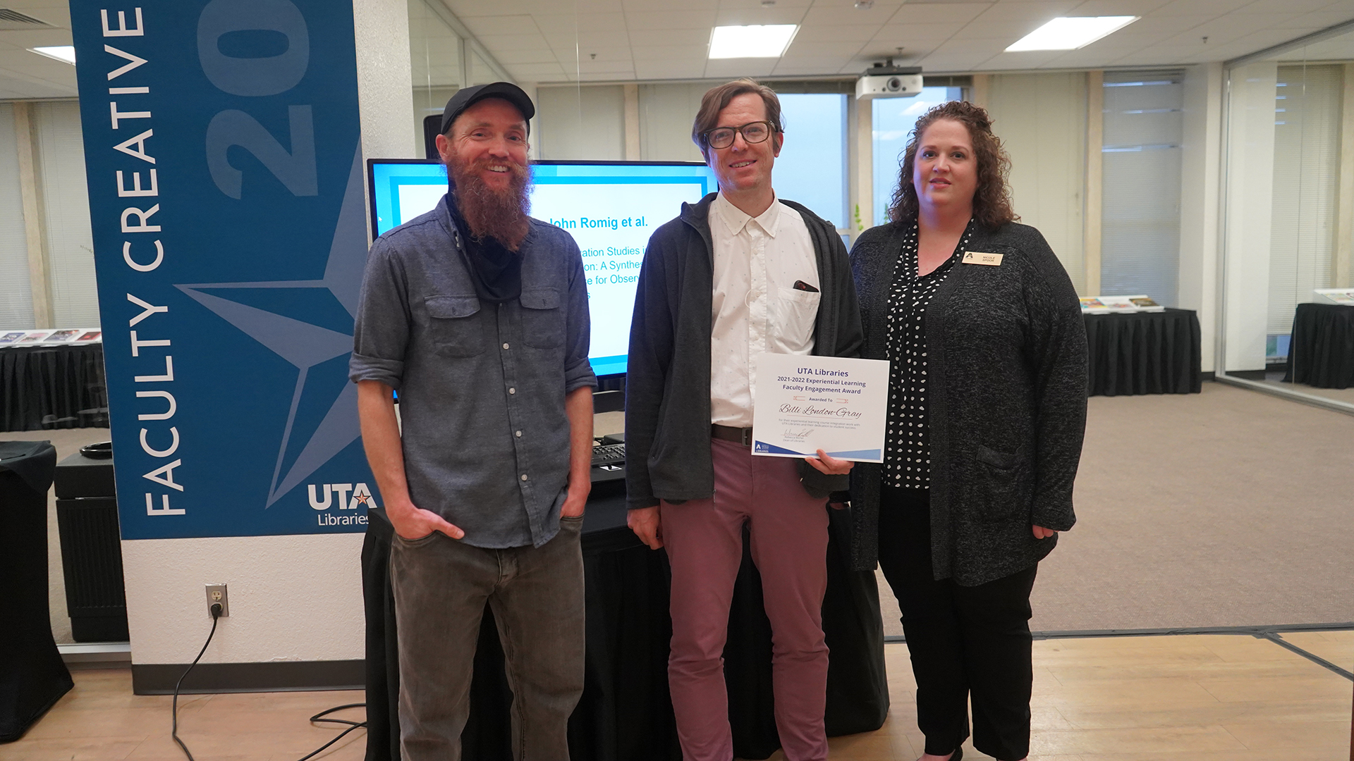 FabLab Librarian Morgan Chivers, Daniel Gray, and Assistant Department Head of Experiential Learning Nicole Spoor pose with a paper award for Billi London-Gray in the Atrium of Central Library.