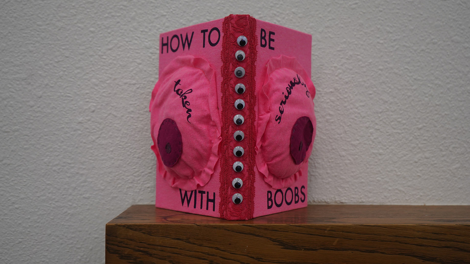 A pink and red art book with simulated breasts and text that reads, "How to be taken seriously with boobs."