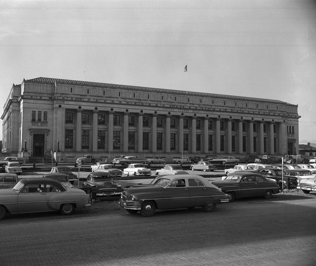 image with 1950s era cars in the foreground and the Fort Worth US Post Office in the background in grayscale.