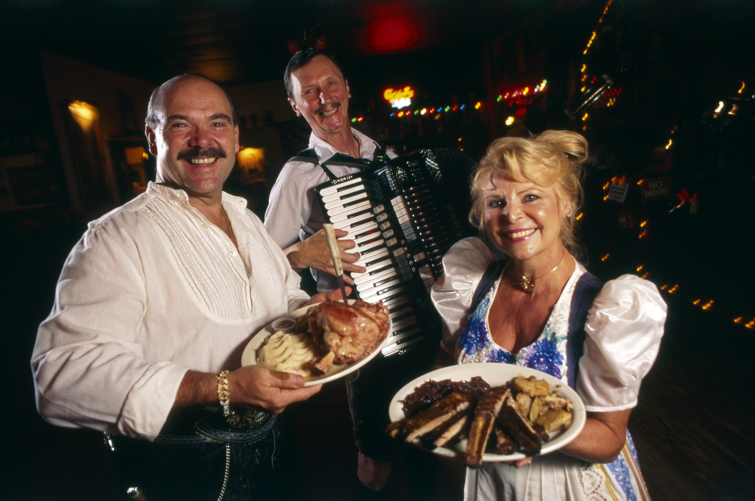 Color photo of three people holding plates of food and a musical instrument.