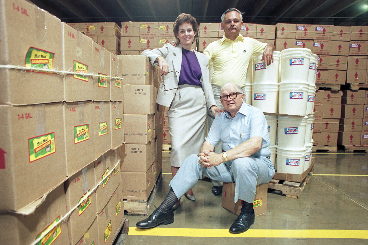 Color photograph of three people pictured in the Best Maid warehouse surrounded by boxes and tubs.