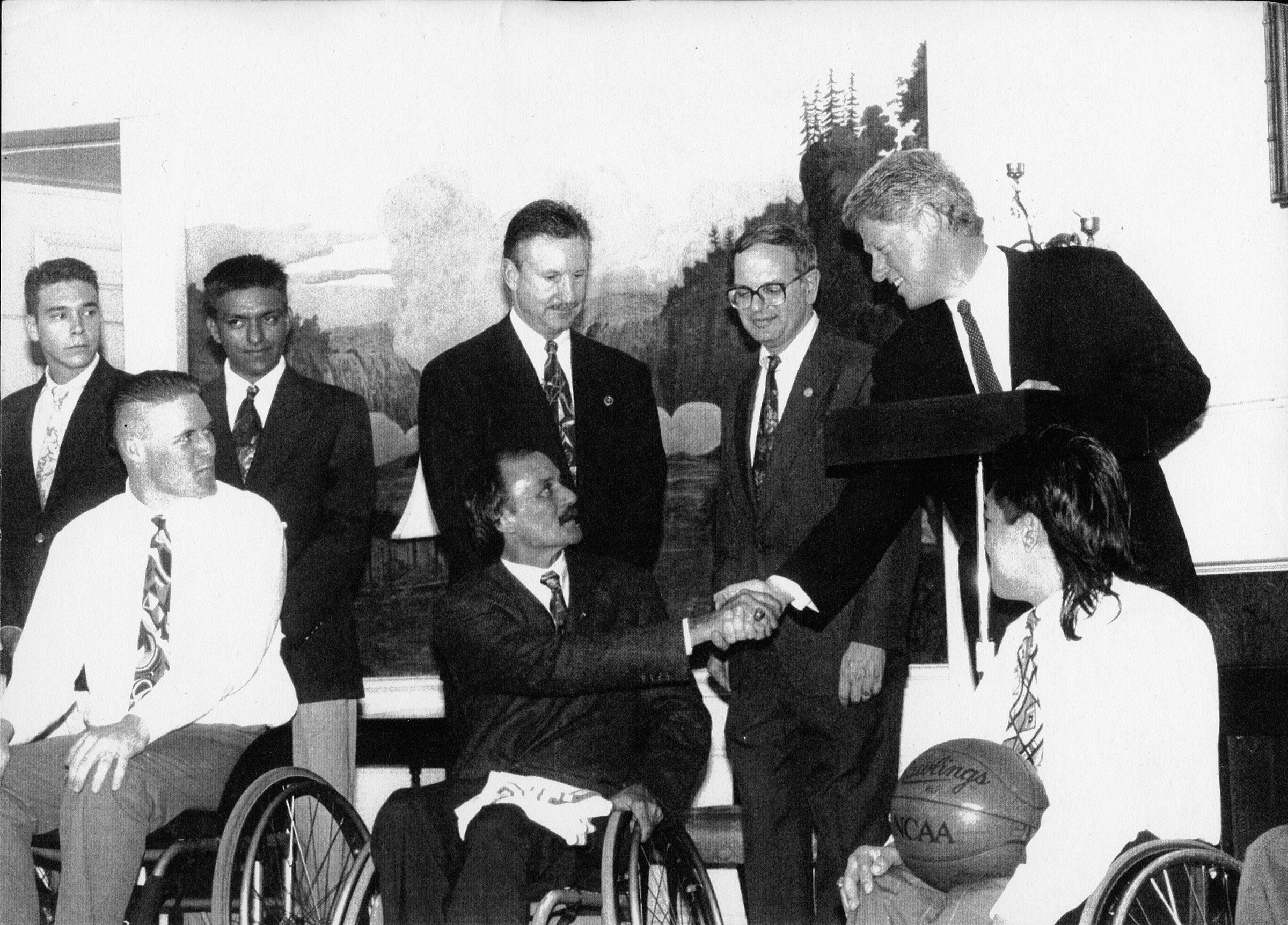 Black and white photo of the UTA Movin' Mavs wheelchair basketball team at the White House with President Bill Clinton shaking hands with coach Jim Hayes.