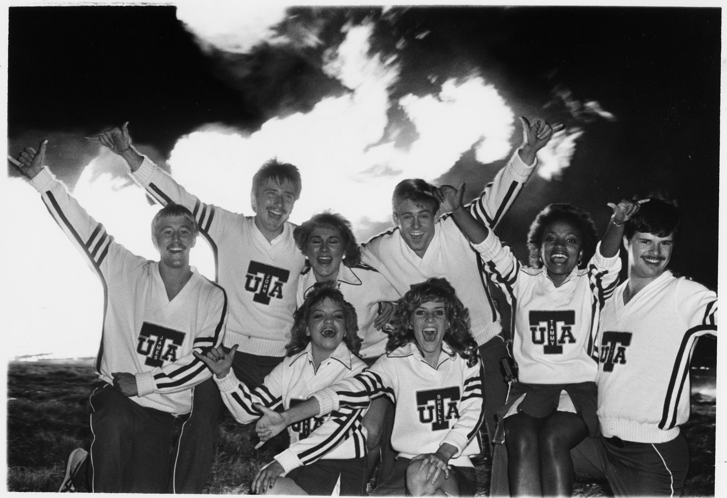 Black and white photo of cheerleaders in front of a bonfire.