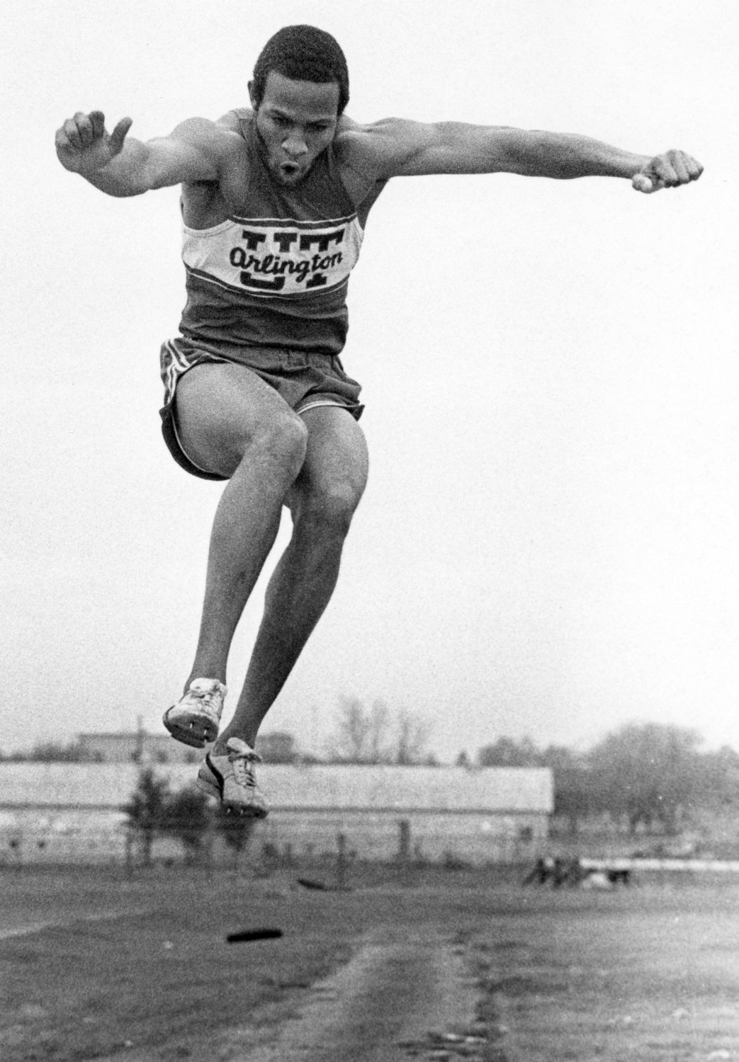 Black and white photo of a track meet with a track member seen jumping.