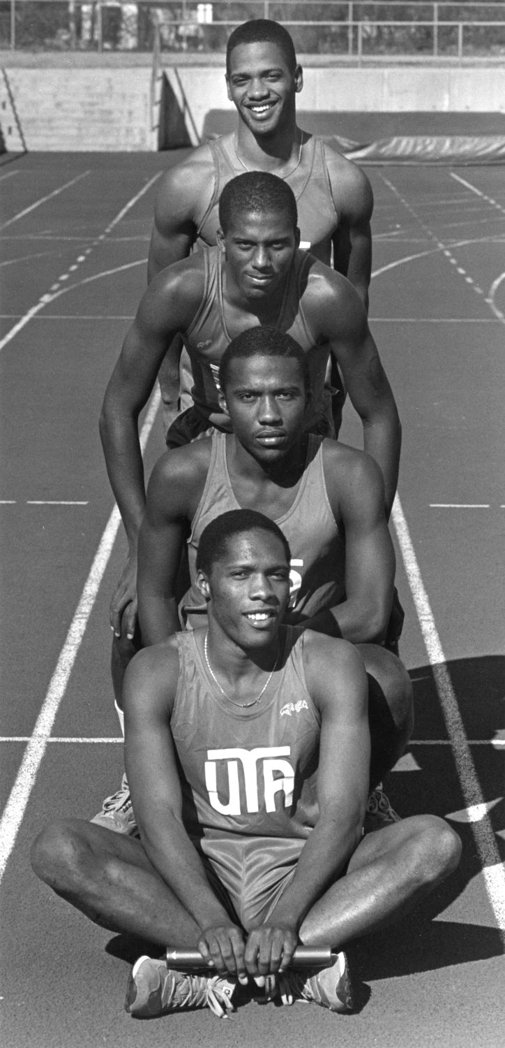 Black and white photo of a group of four men posed on a running track.