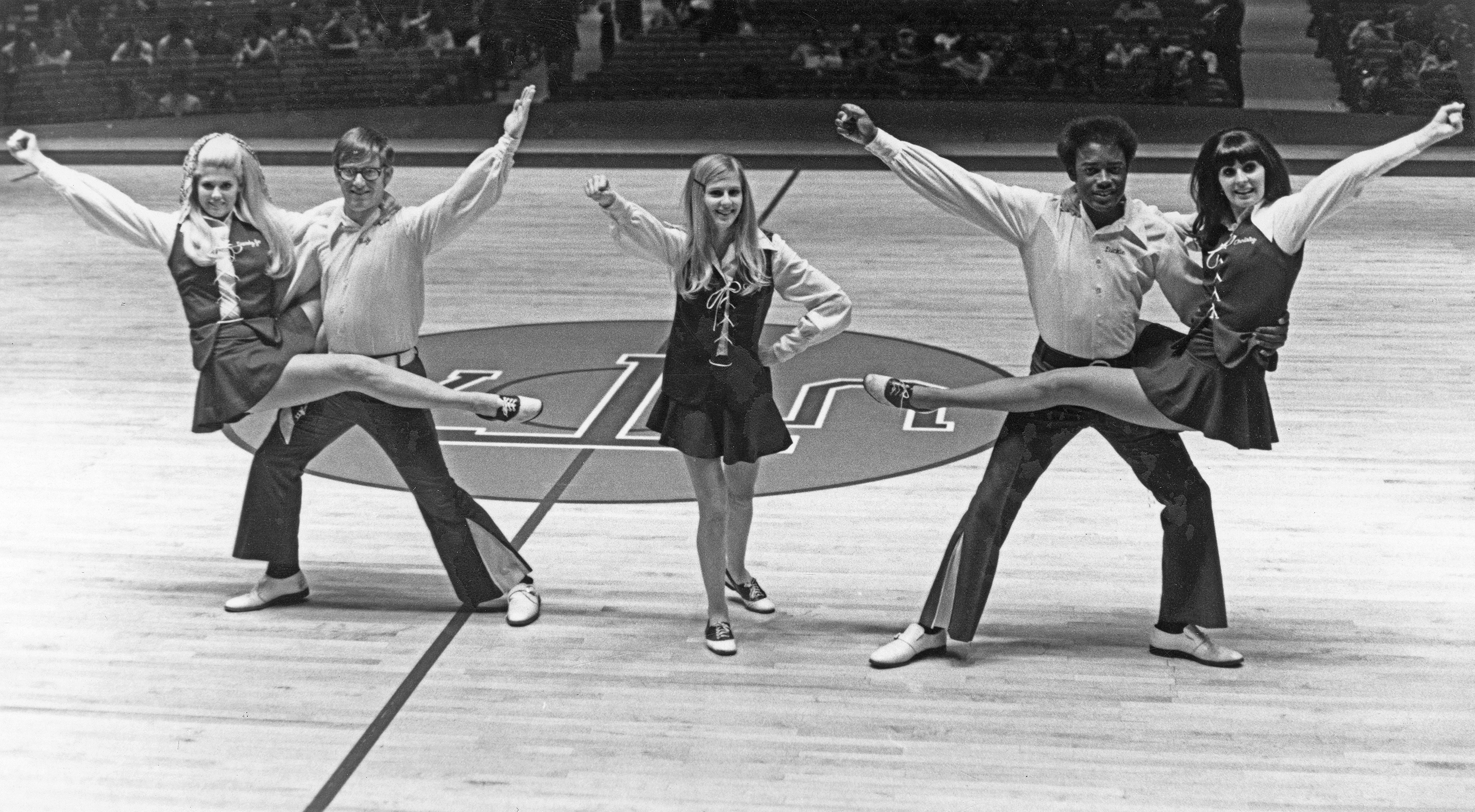 Black and white photo of a group of cheerleaders posed on a basketball court.