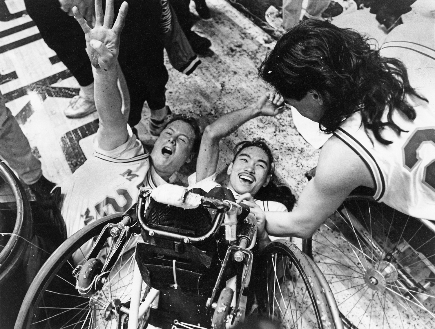 Black and white photo of wheelchairs users celebrating on a basketball court after winning a national title in wheelchair basketball.