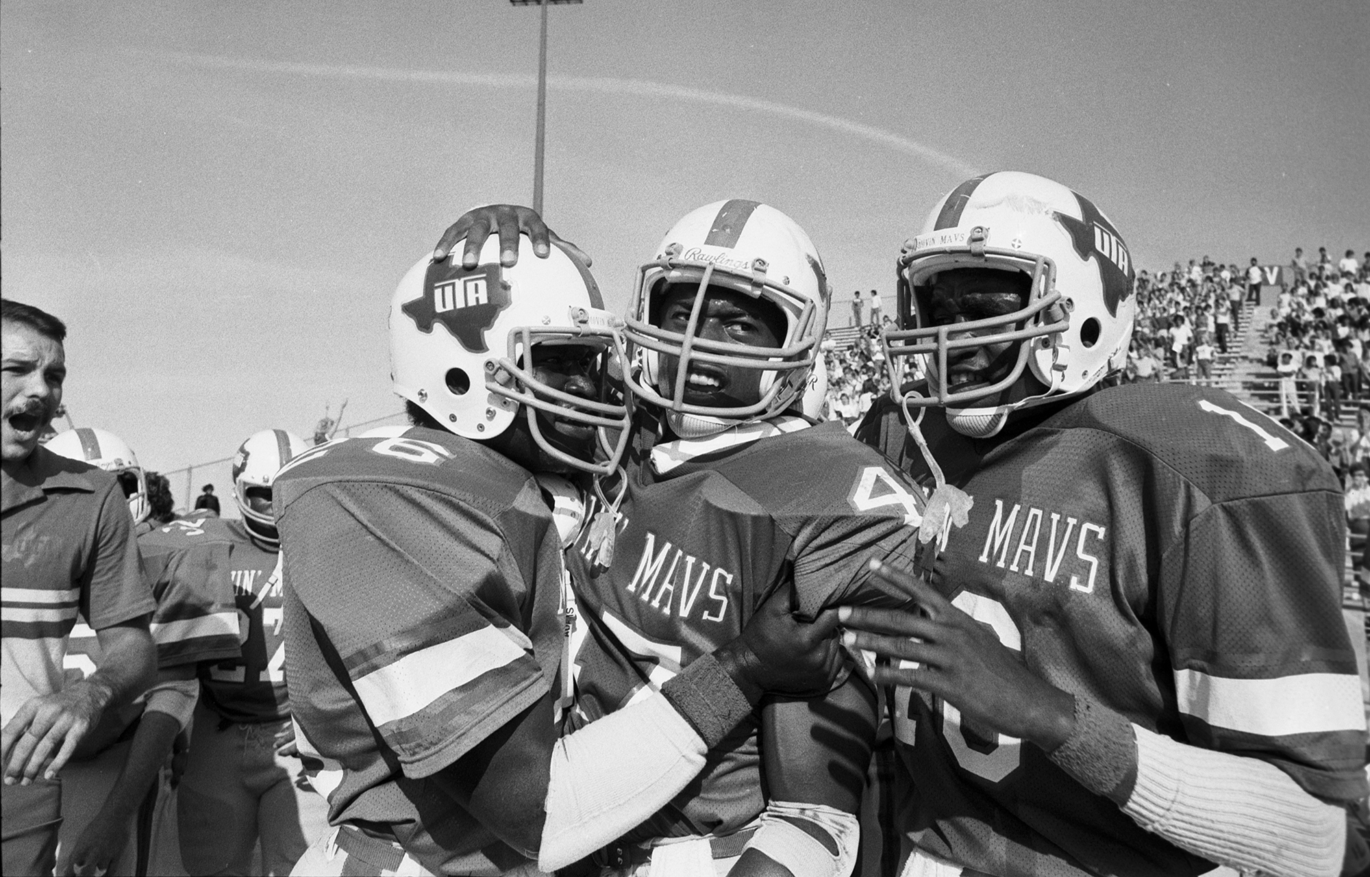 Black and white photo of a group of three football players huddling together in celebration.