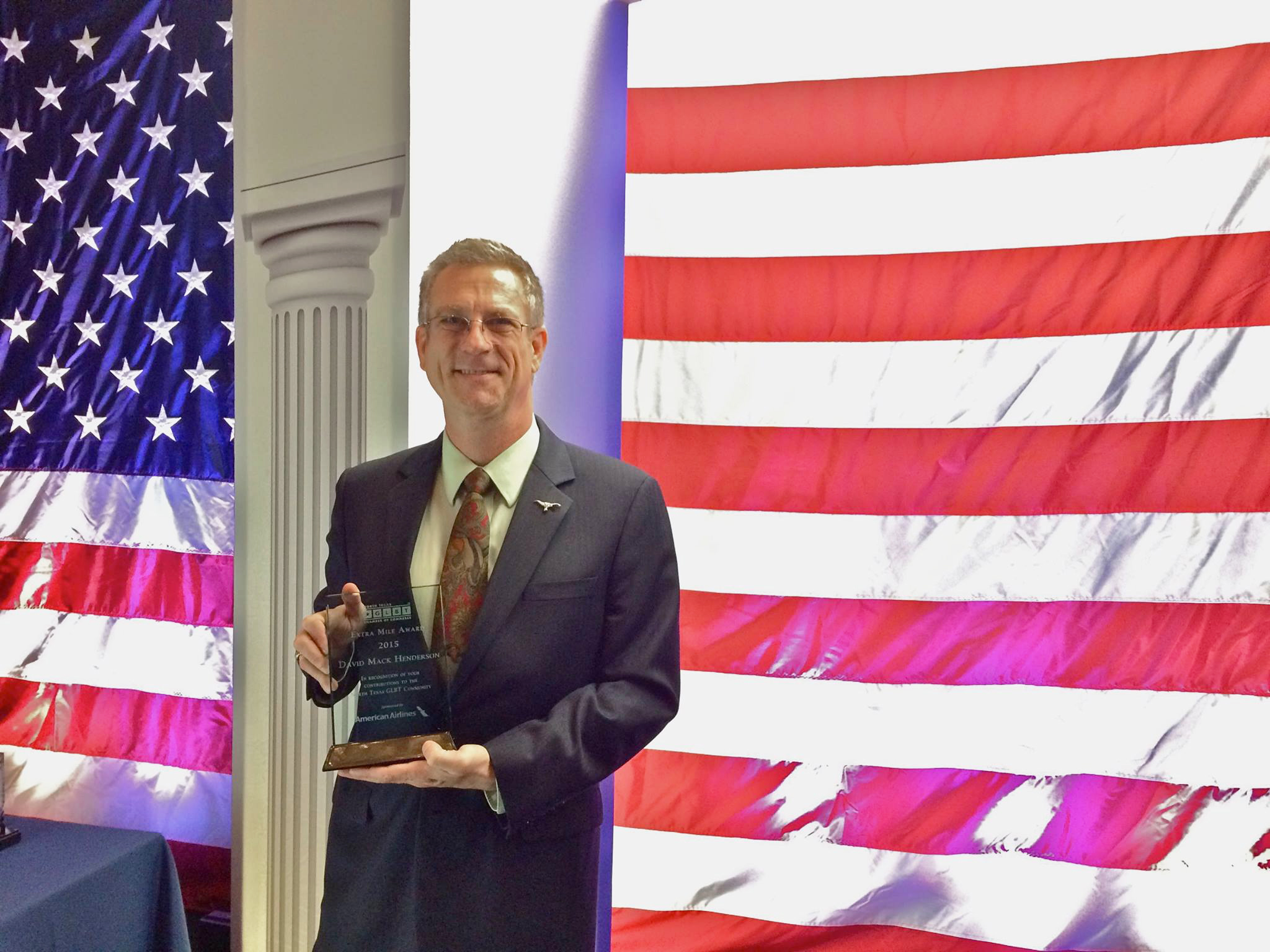 Man holding a glass award in front of an American flag.