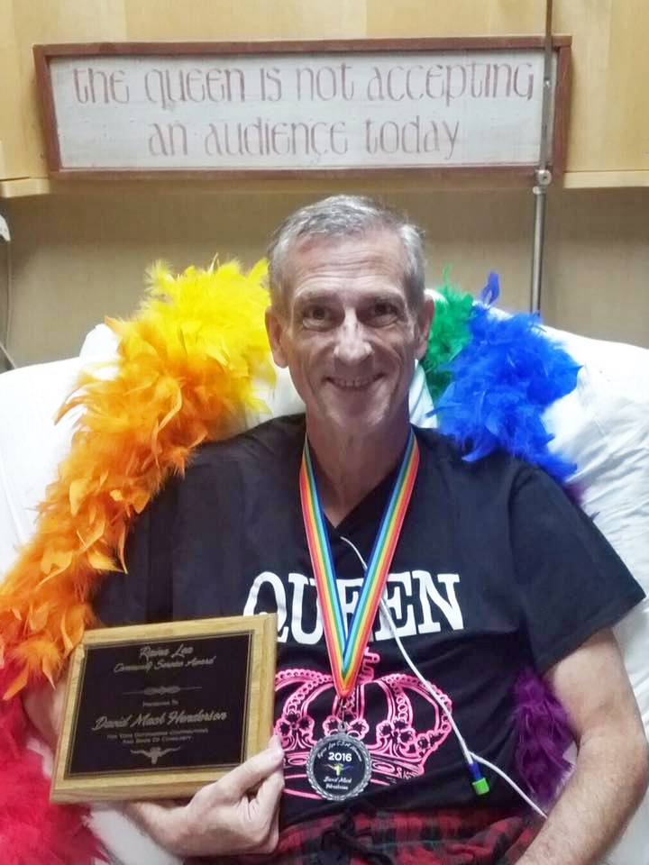 Man surrounded by colorful boa, holding a plaque and wearing a medal.