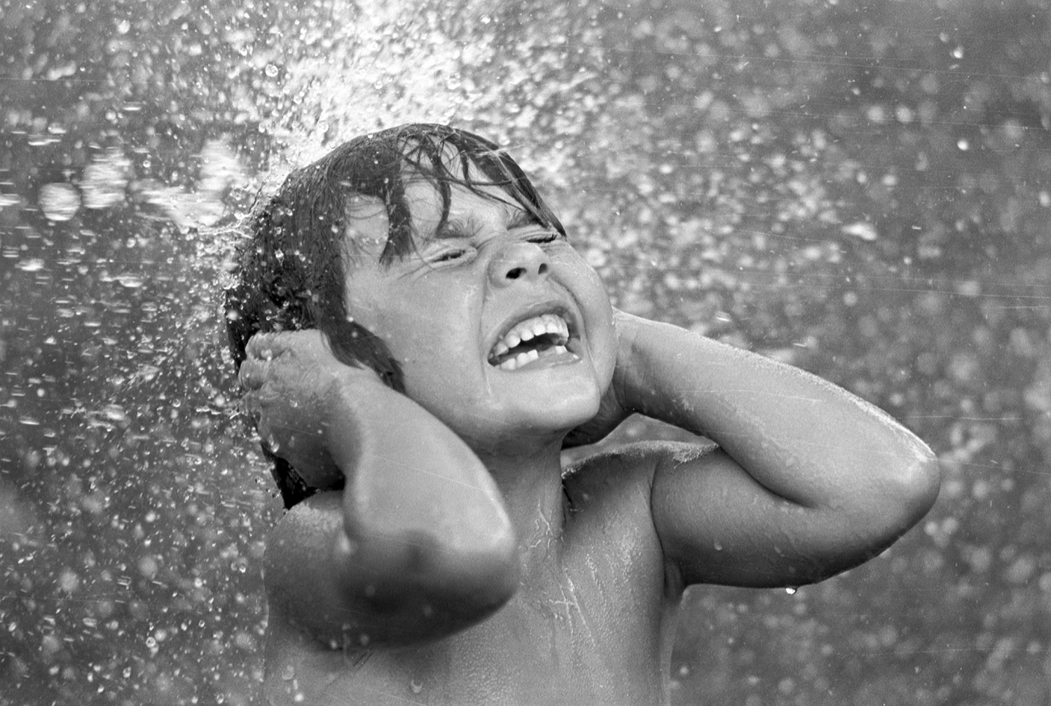 Photo of a young child having water sprayed on them as they covers their ears.