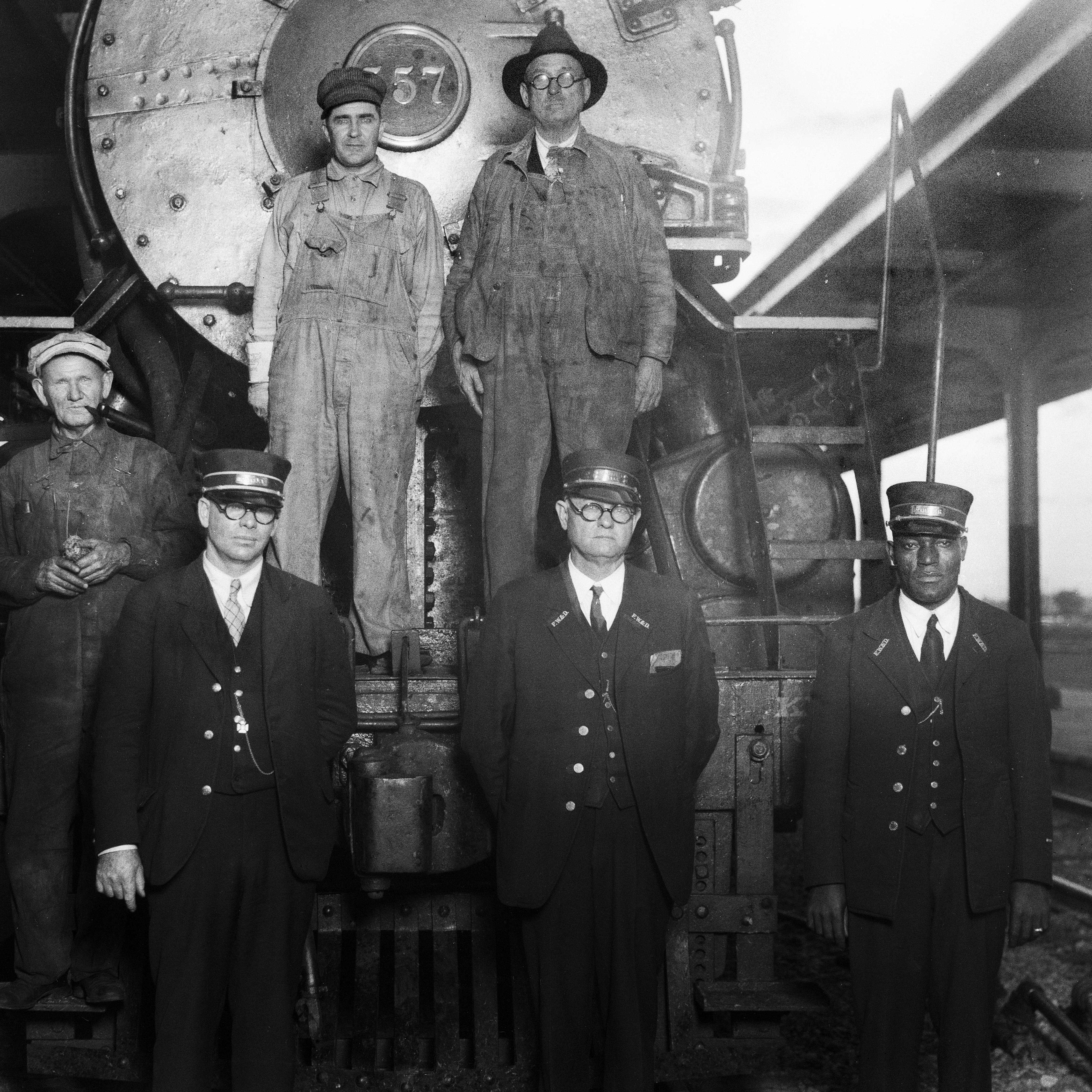 Black and white photo of men who standing in front of a train.