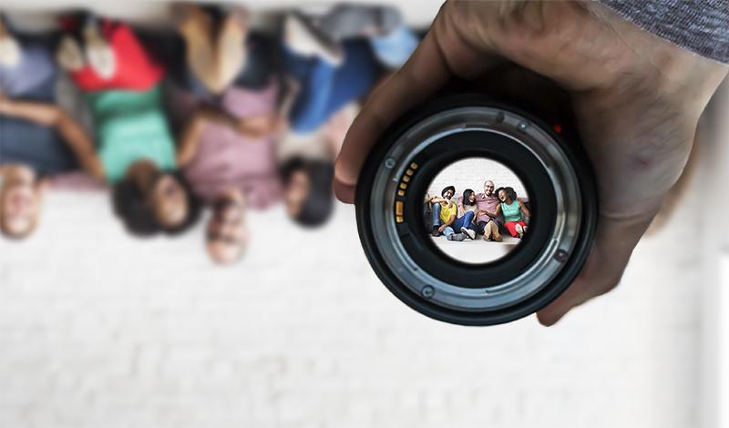 Camera lens displaying diverse group of people right side up, while behind the lens, held by hand, diverse group are out of focus and upside down