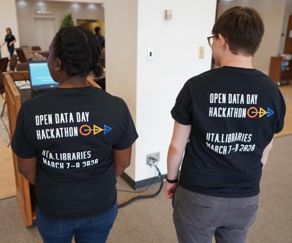 backs of two coordinators, showing the hackathon shirts; "open data day hackathon - UTA Libraries March 7-8 2020"