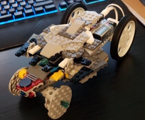 a battery operated car built from lego blocks sits on a desk with a computer keyboard in the background