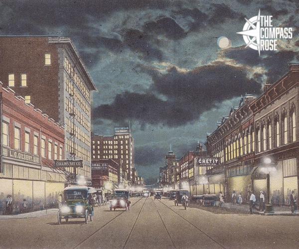 Postcard with Compass Rose logo in top right corner. Looking south on Houston Street from 3rd Street, Fort Worth, Texas. The postcard features a drawing of the street at night with cars in the middle of the street, people walking on the sidewalks, and buildings lining both sides.