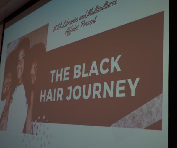 a projection of a slide that reads, "u t a libraries and multicultural affairs present the black hair journey" with a photo of three black women with various styles of hair