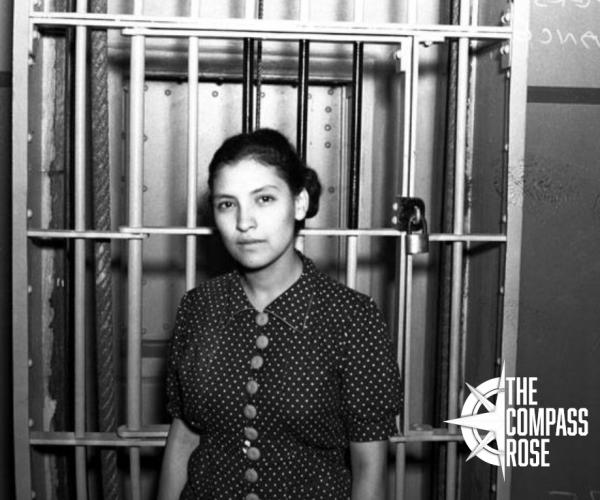 Woman looking directly into the camera in front of a jail cell with "The Compass Rose" logo in the bottom right corner