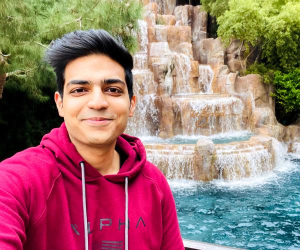 a young man smiles at the camera and poses in front of a waterfall