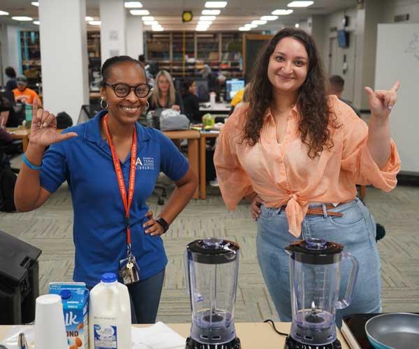Two smiling librarians behind table on which stands blenders and milk