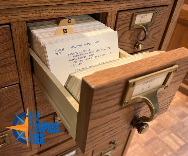 Image of a card catalog with a drawer open and one of the index cards showing. The Compass Rose Logo is in the bottom left hand corner of the image. 